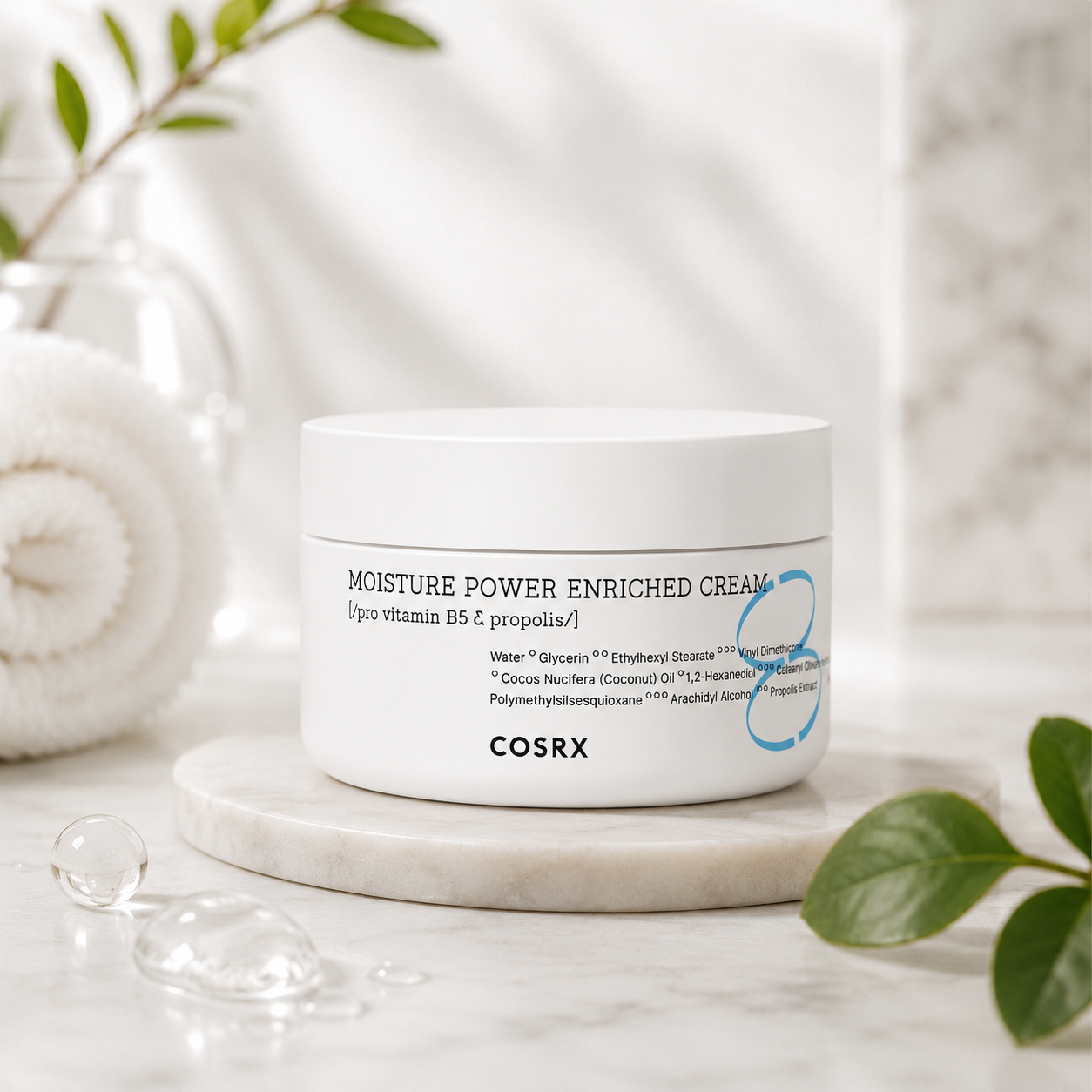 COSRX Full Fit Propolis Light Cream showcased on a marble pedestal with fresh green leaves, a glass vase, a rolled white towel, and clear water droplets, emphasizing hydration and gentle skincare. Formulated with propolis extract and Pro-Vitamin B5, this nourishing facial cream provides long-lasting moisture, calms sensitive skin, supports the skin's protective barrier, enhances a healthy glow, and delivers lightweight comfort for everyday use.